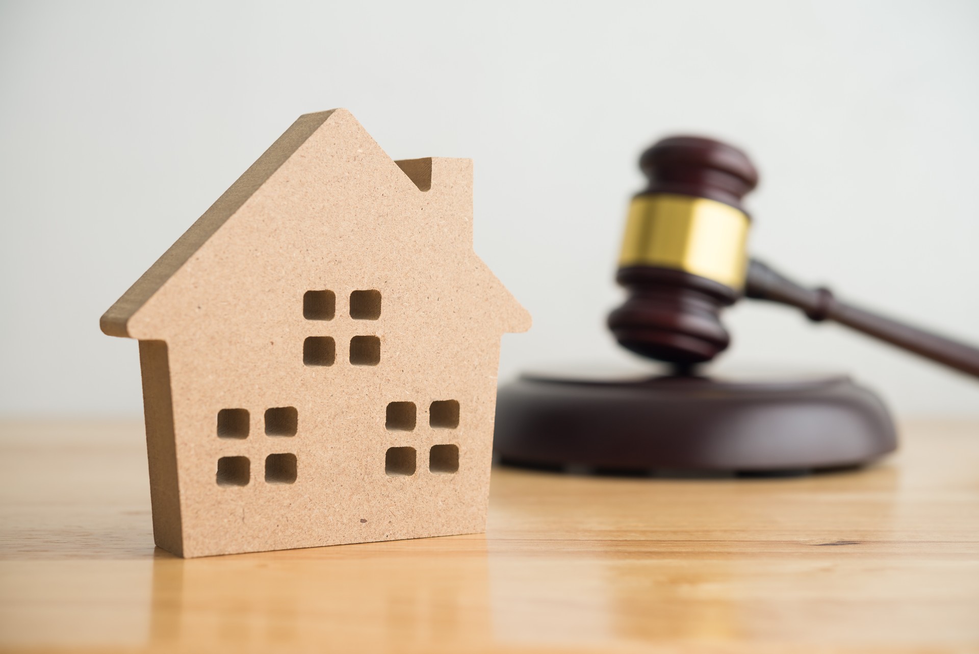 Simple house model, hammer judge gavel on wooden table with white wall background.